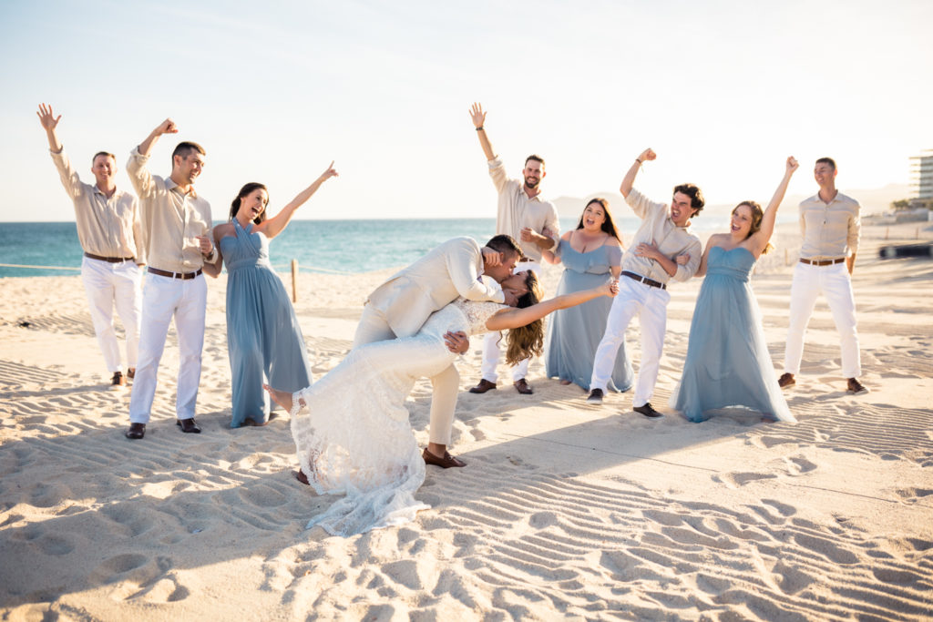 wedding party cheering while bride and groom kiss on beach