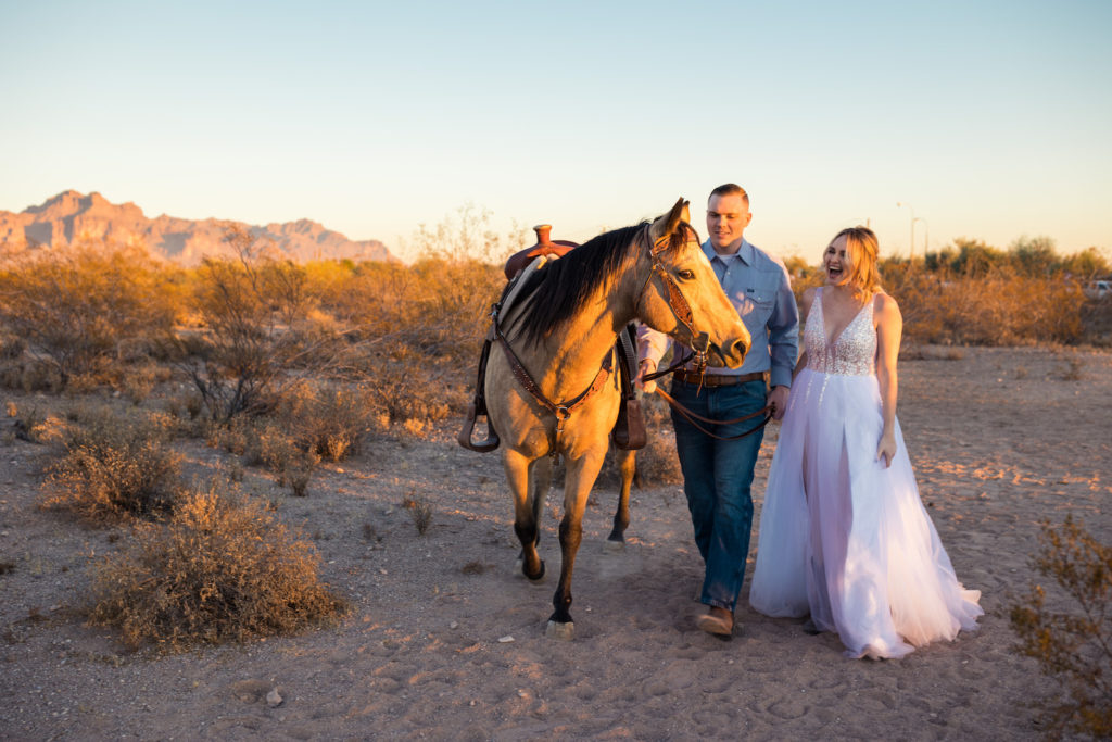 A bride and groom smile while walking with a horse during their desert elopement photographed by Makayla McGarvey.