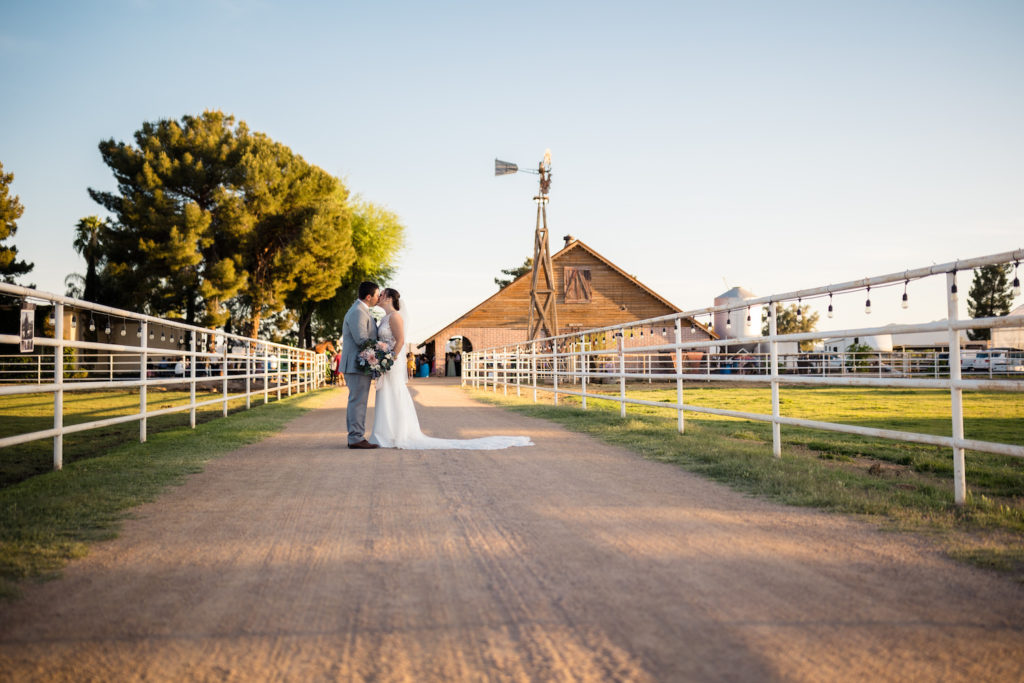 A bride and groom kiss while standing on the road next to a horse pasture, photograph by Makayla McGarvey.