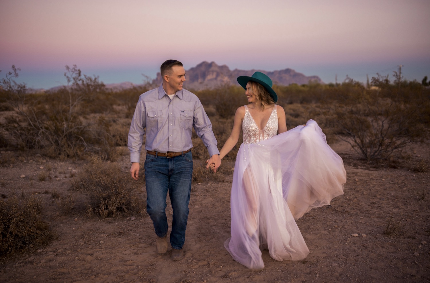 A bride and groom hold hands while walking in the desert during their adventure elopement photographed by Makayla McGarvey