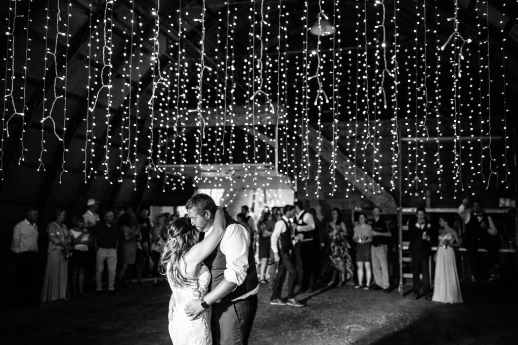 Black and white photo of the bride and groom dancing under fairy lights after their ranch wedding ceremony