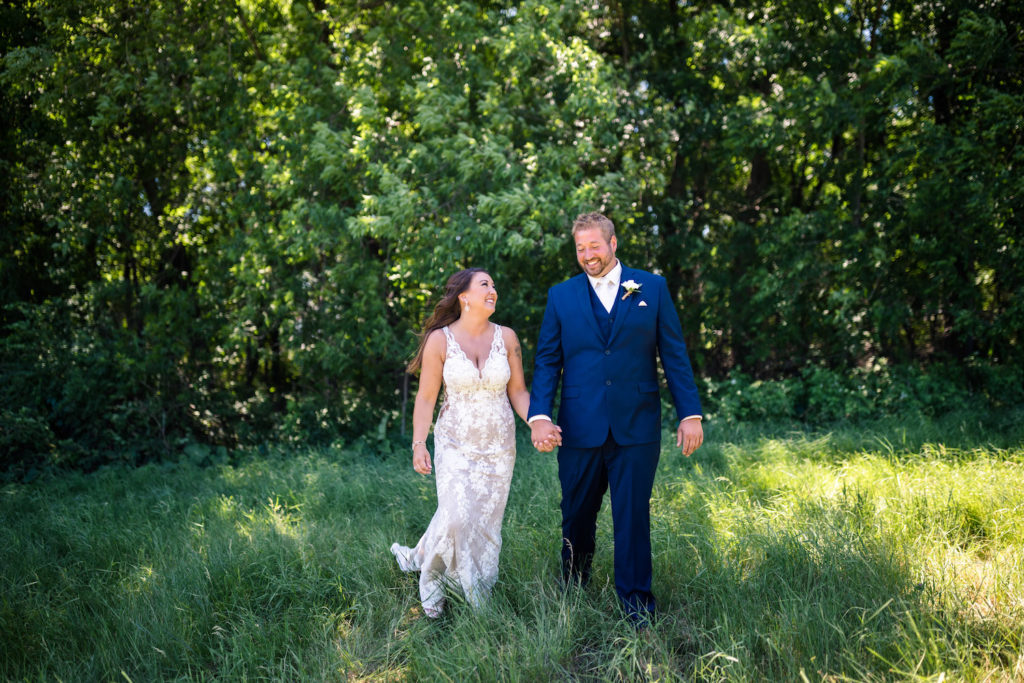 Bride and groom hold hands as they stroll around the lush greenery at their ranch wedding location