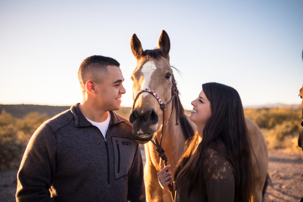 Couple share a smile as the look at their horse during their engagement session, taken by Makayla McGarvey Photography