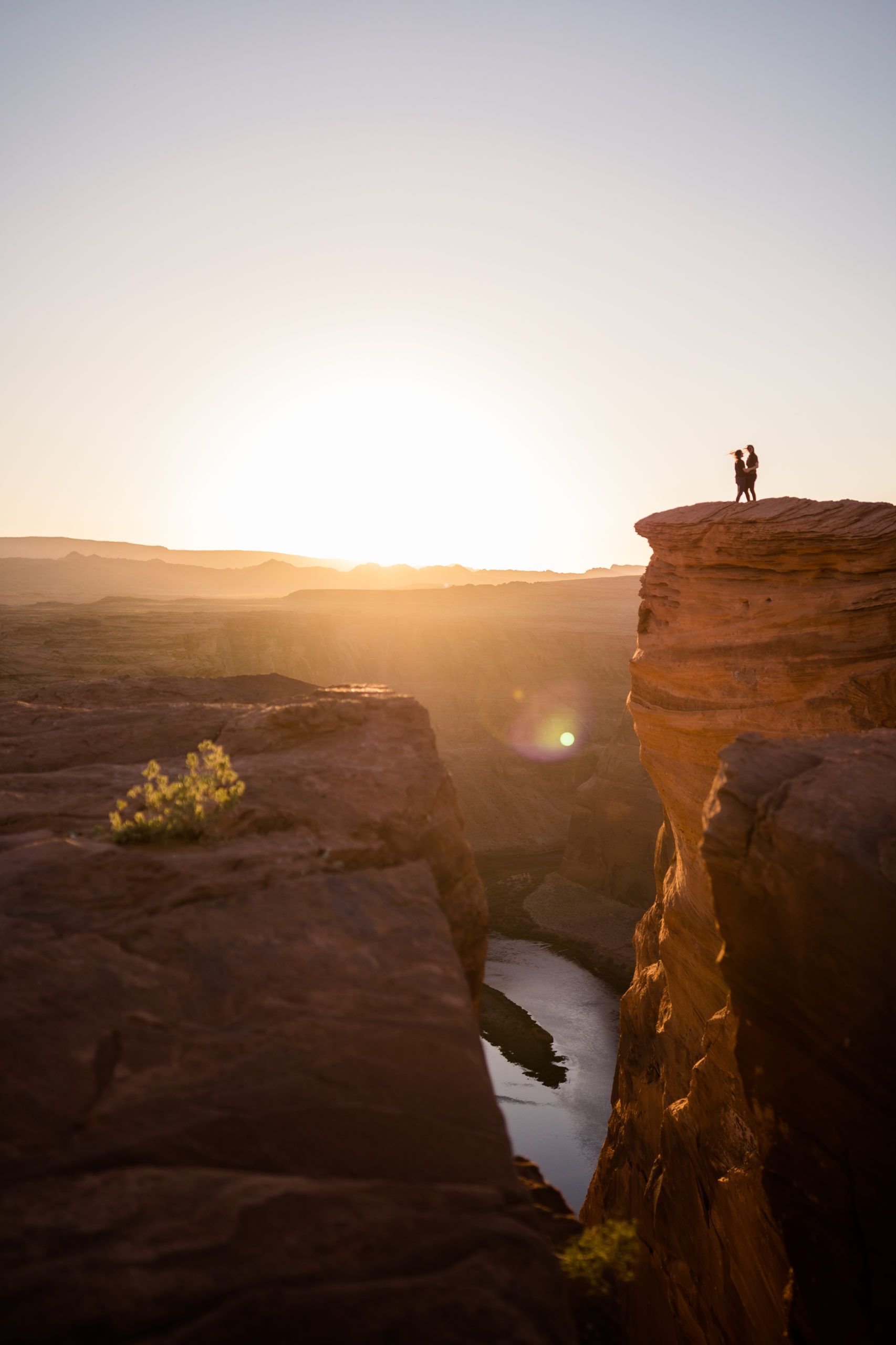 Couple out on the top of lookout at Horseshoe Bend with the view of the sun in the horizon 