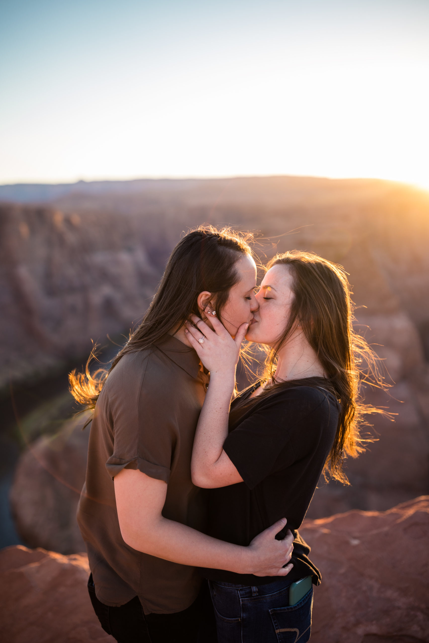 Couple sharing a kiss with the sun coming up behind them at Horseshoe Bend during their proposal