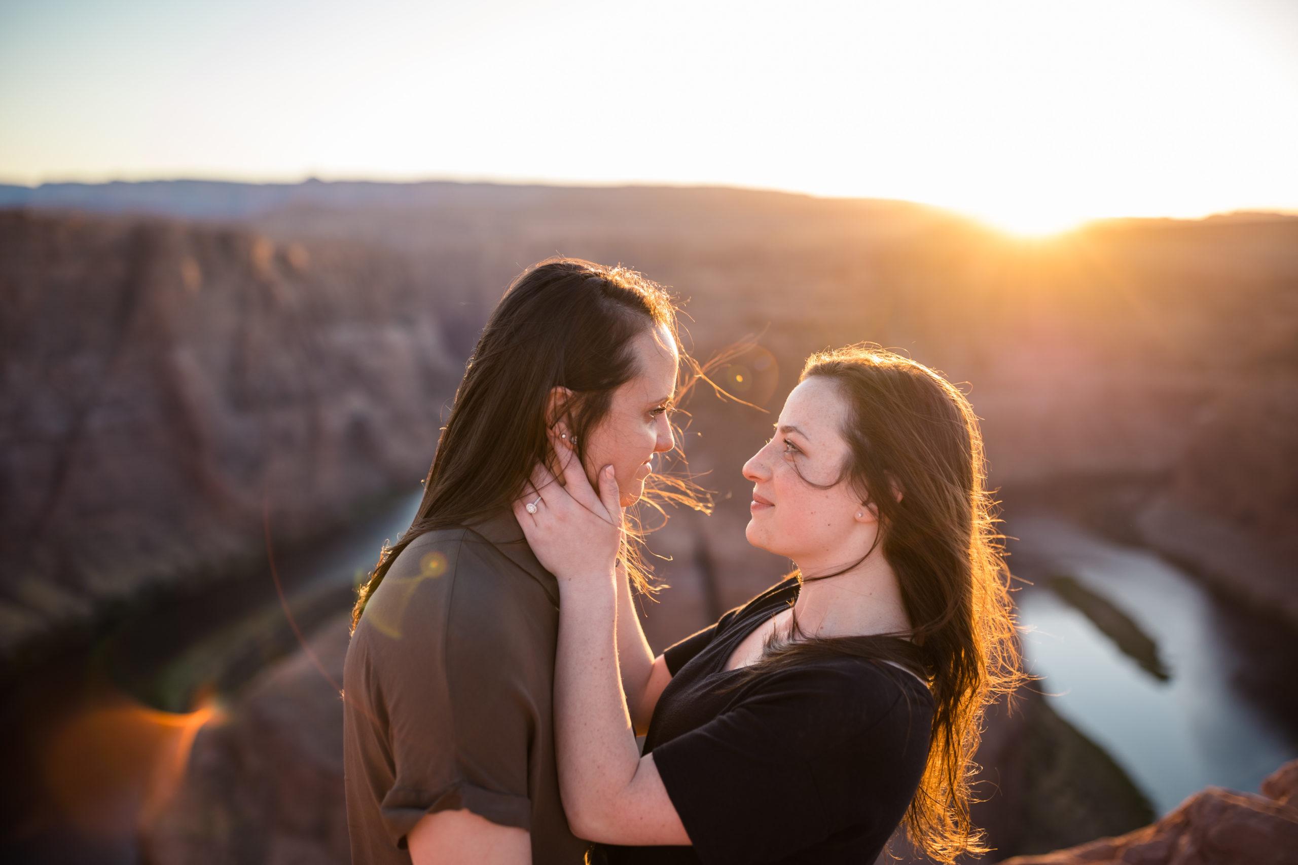 Couple looking at each other endearingly, with a breathtaking view of the sun and of Horseshoe Bend behind them, captured by Makayla MacGarvey