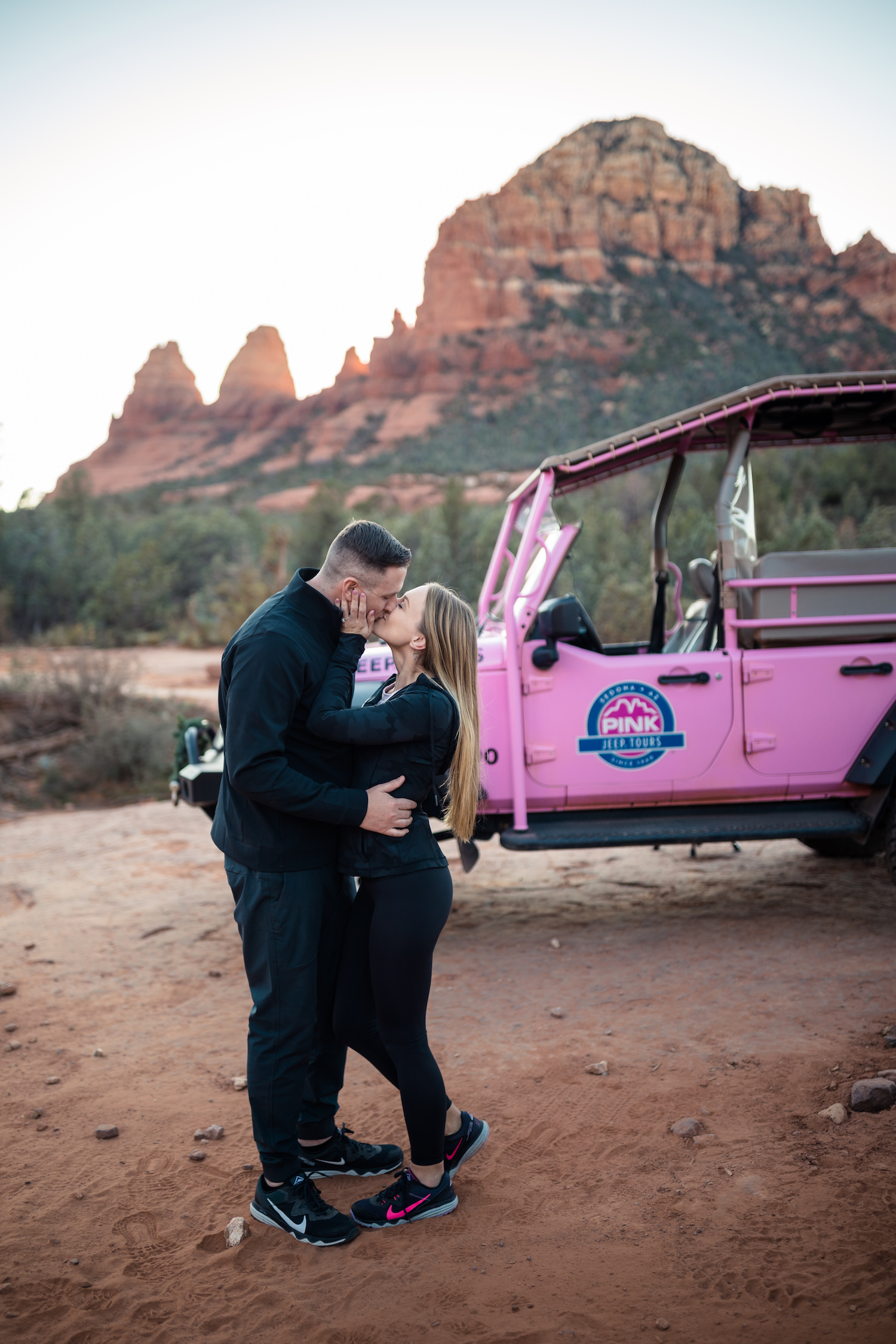 Newly engaged couple sharing a kiss in front of the Pink Jeep during their proposal, photographed by Makayla MacGarvey