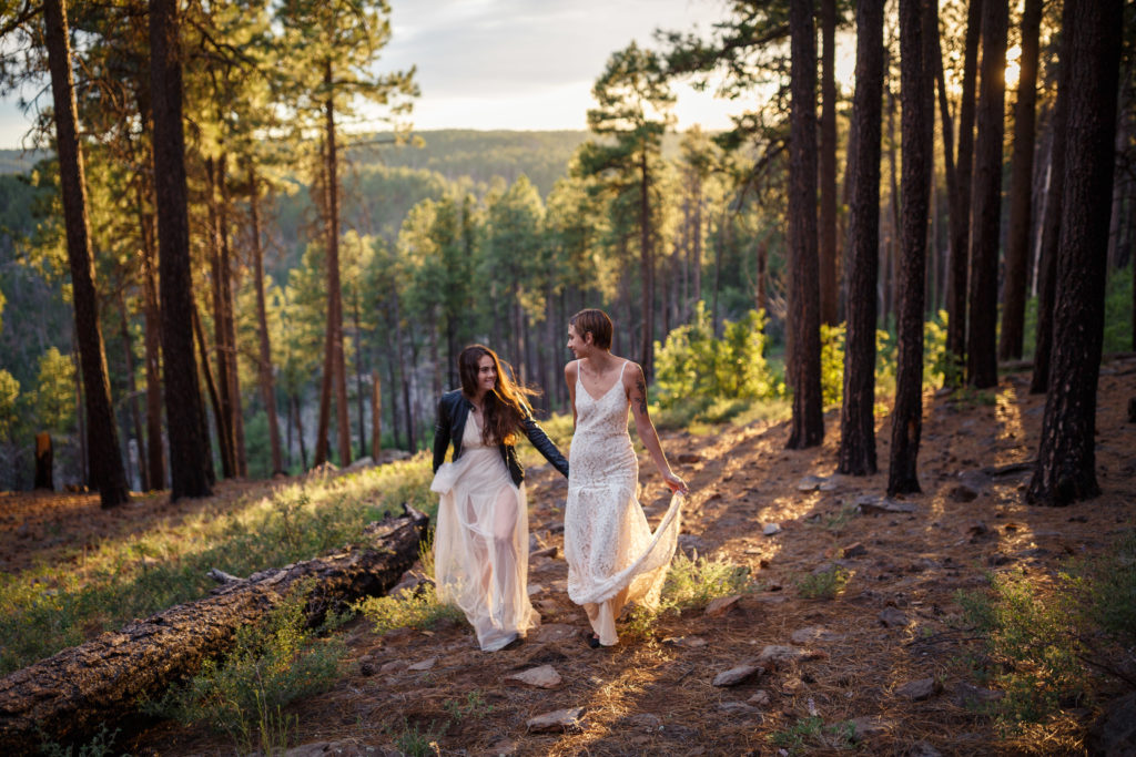 two brides holding hands while walking through the forest