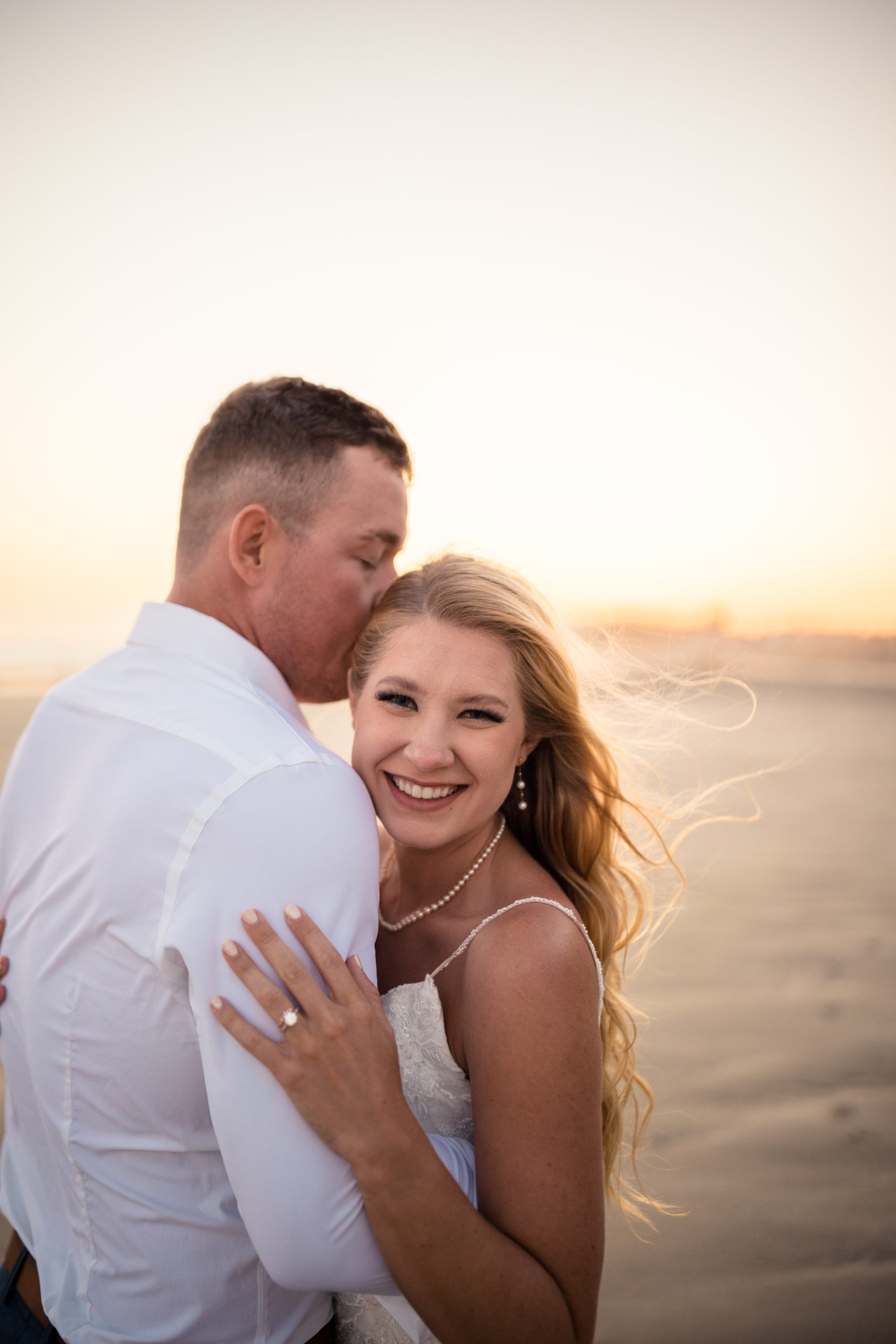 groom kissing bride on beach at sunset