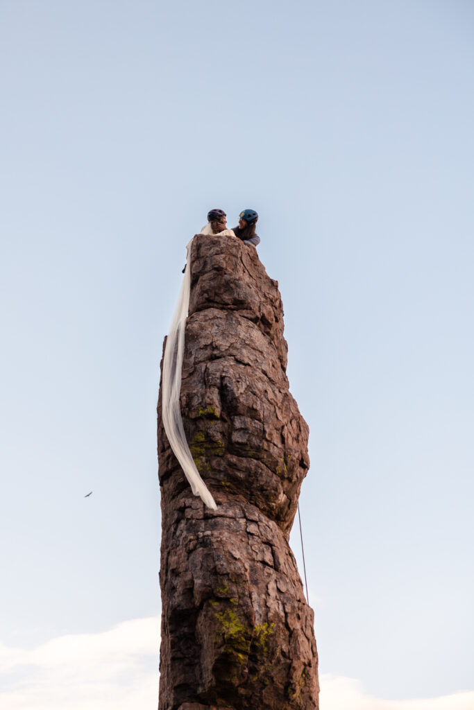 A bride and groom sitting at the top of Totem Pole after rock climbing on their wedding day.