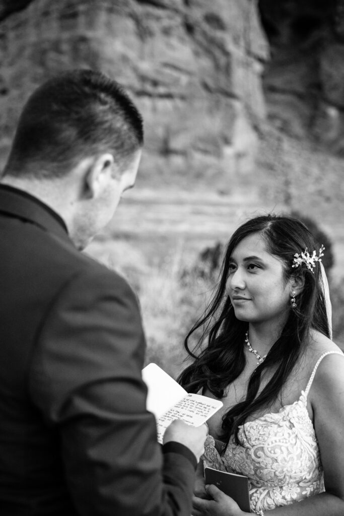 An Arches National Park elopement ceremony. The groom is reading his vows as the bride looks at him.