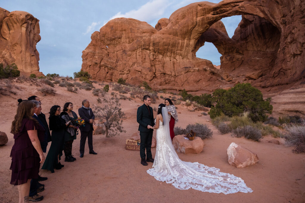 An Arches National Park elopement ceremony. The couple is facing each other and holding hands, while the officiant reads. Their guests are standing next to them, lined up.