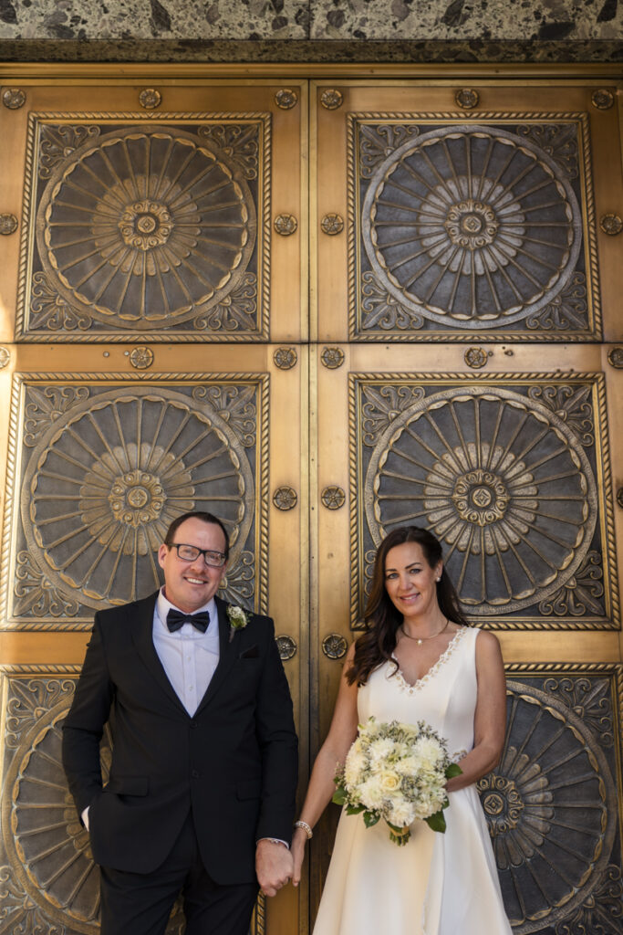 bride and groom smiling in front of courthouse doors