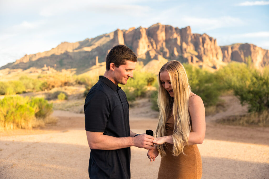 One of the best places to propose in Phoenix is the Superstition Mountains. A man is putting an engagement ring on his partner's fingerafter popping the question.