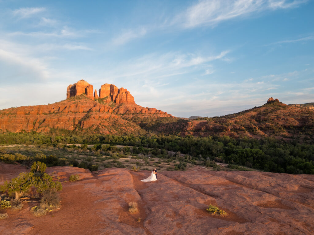 A wide view of Secret Slick Rock, and a couple standing on it, with Cathedral Rock in the backdrop.