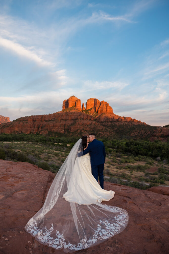 A couple is at Secret Slick Rock on their elopement day, facing Cathedral Rock but looking at each other, with the bride's veil behind her.