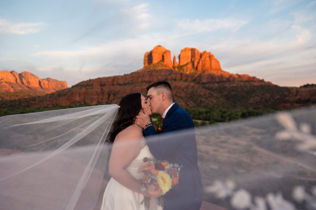 A couple is at Secret Slick Rock on their elopement day, kissing while the bride's veil blows in the wind.