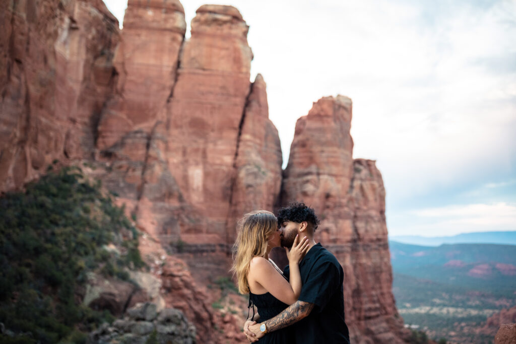 A couple standing on the ledge at Cathedral Rock, kissing each other on their elopement day.