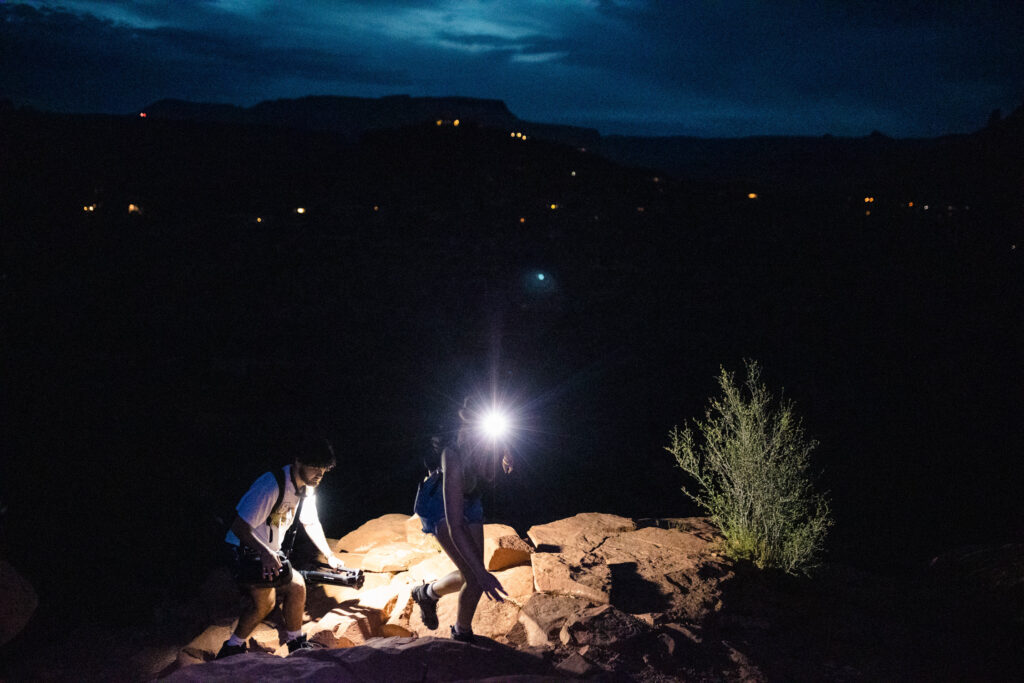 A couple hiking the Cathedral Rock trail early in the morning. It is dark, with their headlamps illuminating the way.