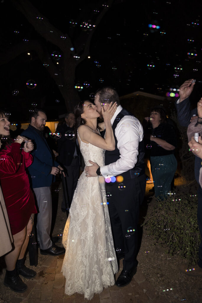 bride and groom kissing during grand getaway with bubbles in the air