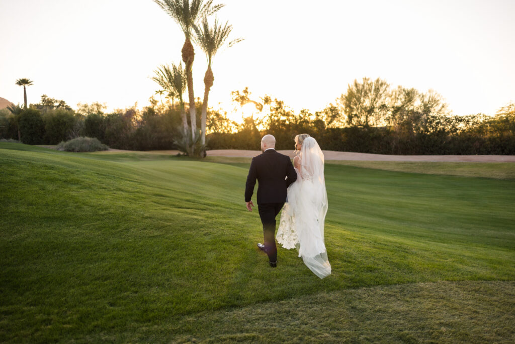 A couple walking on the golf course at the Mountain Shadows Resort as the sun sets, dressed in their wedding attire.