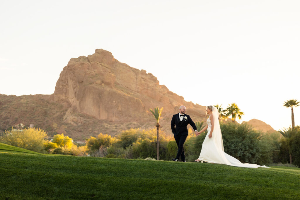 A couple walking across the golf course at the Mountain Shadows Resort, dressed in their wedding attire.