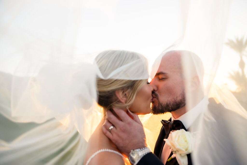 Bride and Groom kissing under veil at golf course wedding.